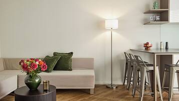 A modern living room with a sofa, a round table with a vase of flowers, a floor lamp, and a dining area with bar stools.
