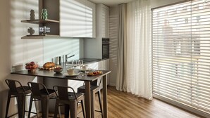 A modern kitchen with a central island, bar stools, and a large window with blinds. - Base Geneva (Geneva)