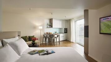 Una habitación de hotel con una cama grande, un escritorio pequeño, kitchenette y un ventanal amplio.