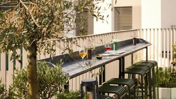 Une terrasse avec une longue table, deux verres de vin et des tabourets de bar verts.