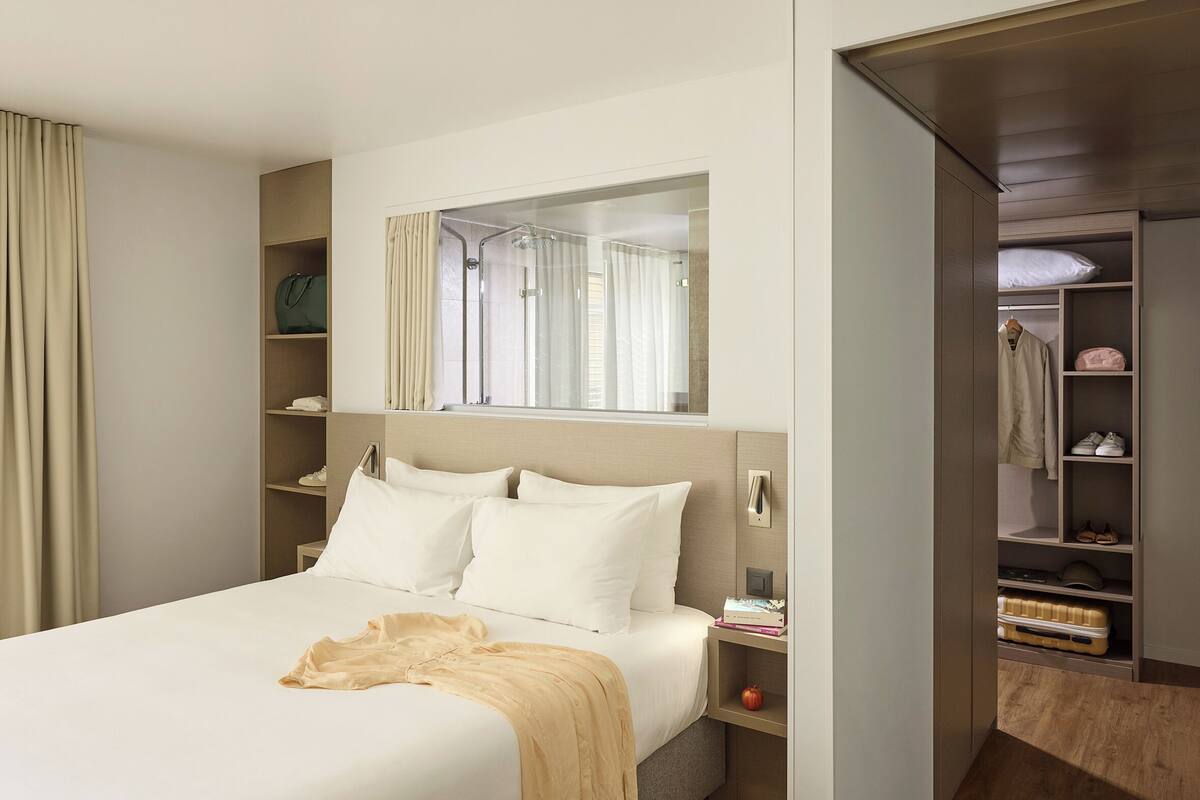 Une chambre d’hôtel comprenant un lit, une table de chevet, un miroir, une armoire et un espace douche.