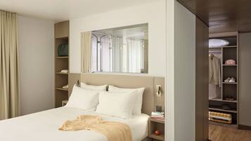 A hotel room with a bed, a bedside table, a mirror, a wardrobe, and a shower area.