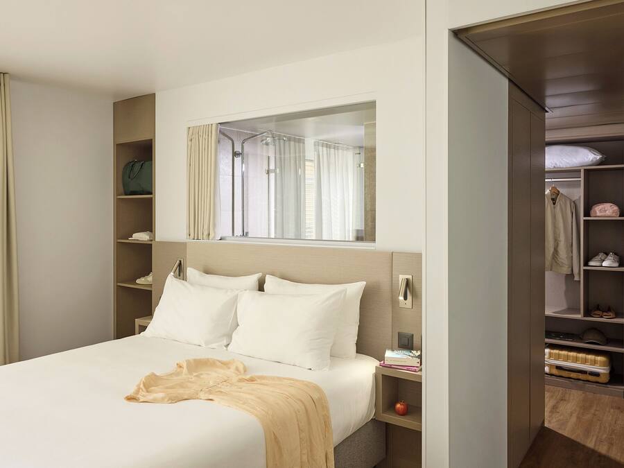 A hotel room with a bed, a bedside table, a mirror, a wardrobe, and a shower area.