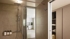 A modern bathroom with a shower, a glass door leading to a bedroom, and a wardrobe with a suitcase. - Base Geneva (Geneva)