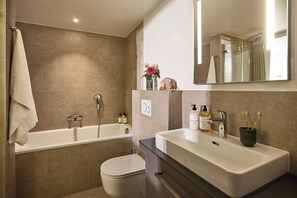 A modern bathroom with a bathtub, toilet, and a large sink with a mirror above.