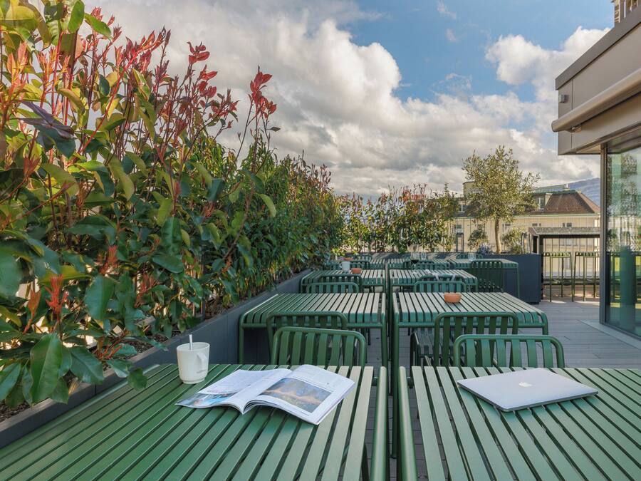 An outdoor seating area with green tables and chairs, a magazine, and a laptop.