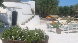 A white building with a conical roof, a stone staircase, and a garden area with benches and potted plants. - Trullo The Magnificent (Ostuni)