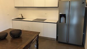 A modern kitchen with white cabinets, a stainless steel refrigerator, a water dispenser, and a wooden dining table with two chairs. - Trullo The Magnificent (Ostuni)