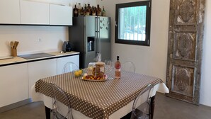 A kitchen with white cabinets, a stainless steel refrigerator, a dining table with a polka dot tablecloth, and a rustic wooden door. - Trullo The Magnificent (Ostuni)