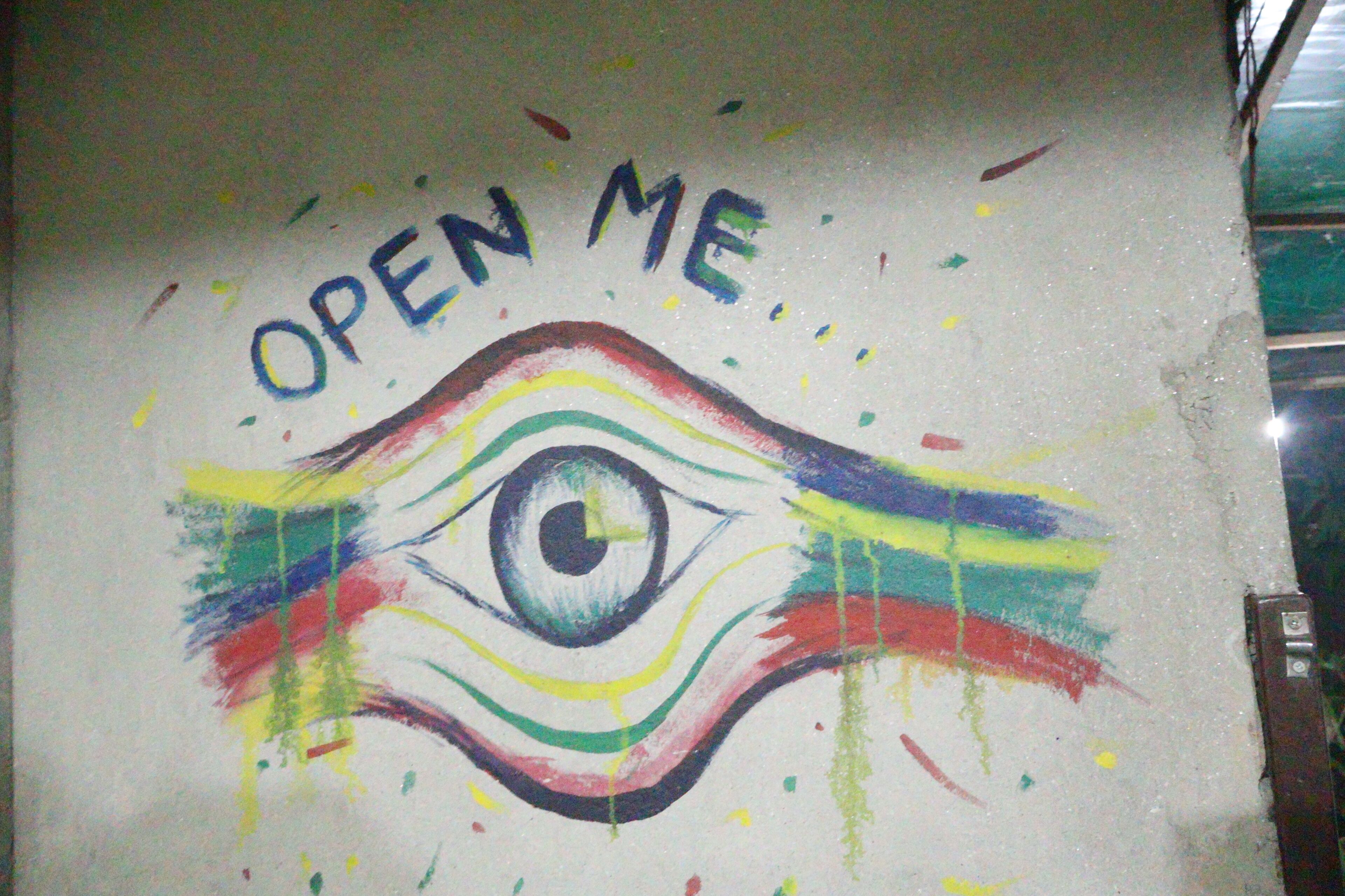 A wall with a colorful eye and the text 'OPEN ME' written above it.