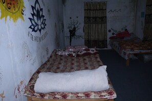 Una habitación con una cama, otra cama al fondo, un muro con grafitis y un adorno con forma de árbol.