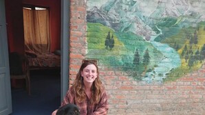 Une personne assise par terre, à côté d’un chien, devant une fresque représentant un paysage de montagne.