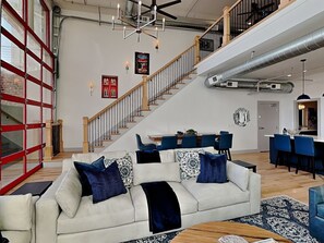 Un vaste espace de vie comprenant un canapé blanc, des coussins bleus, une table à manger et un escalier.