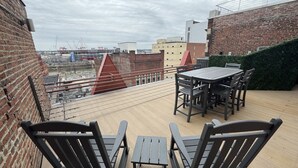 Terraza en la azotea con mesa y sillas, vista panorámica de la ciudad y un muro de ladrillo.