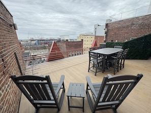 A rooftop terrace with a table and chairs, a view of the cityscape, and a brick wall.