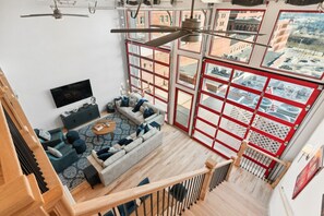 Een woonkamer met hoge plafonds, een grote bank, een salontafel en een televisie.