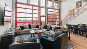 A spacious living room with a large window, a sofa set, a coffee table, and a staircase. - Majestic Lofts #601 - Penthouse (Nashville)