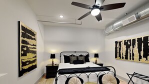 Un dormitorio con cama, dos mesitas de noche, ventilador de techo y obras de arte en las paredes.