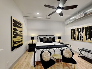 A bedroom with a bed, two bedside tables, a ceiling fan, and artwork on the walls.