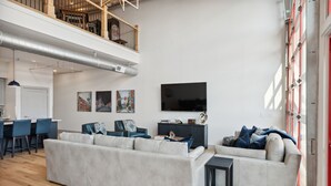 Un grand espace de vie comprenant un grand canapé, une table à manger et un téléviseur. Un escalier mène à un niveau supérieur.