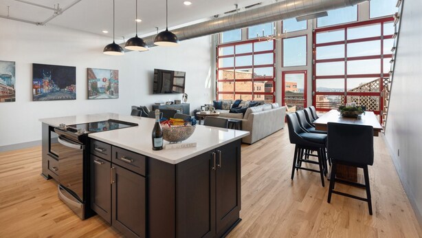Una cocina moderna con una isla central, un comedor con mesa y sillas, y una sala de estar con sofá y televisor.