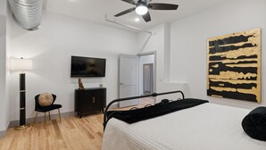 Une chambre à coucher avec un lit, un ventilateur de plafond, une télévision, une armoire et un tableau.