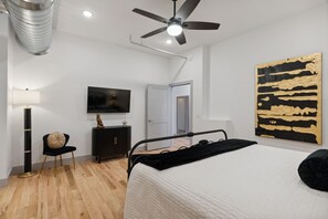 A bedroom with a bed, a ceiling fan, a TV, a cabinet, and a painting. - Majestic Lofts #601 - Penthouse (Nashville)