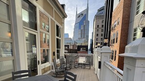 Un patio al aire libre techado con una mesa y sillas, una cerca blanca y vistas a un edificio alto al fondo.