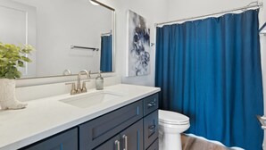 Un baño moderno con un lavamanos blanco, muebles oscuros, un inodoro blanco y una cortina de ducha azul.