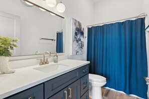 A modern bathroom with a white sink, dark cabinets, a white toilet, and a blue shower curtain.