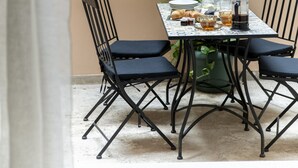 A table with four chairs, a window with metal bars, and a potted plant. - 2BR Greek Home | Private Backyard 20' to Acropolis (Athens)