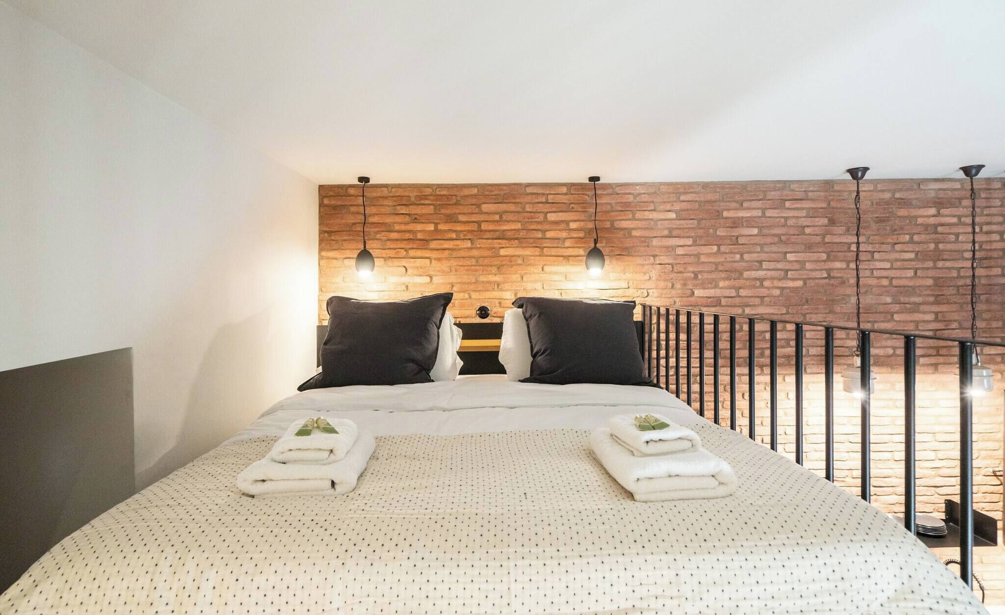 A bed with a white quilt, two black pillows, and two folded towels with green leaves.