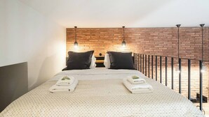 A bed with a white quilt, two black pillows, and two folded towels with green leaves. - 1BR Boutique Apt Acropolis Rooftop view (Athens)