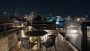 A rooftop terrace with a round table and chairs, overlooking a cityscape at night. - 1BR Boutique Apt Acropolis Rooftop view (Athens)