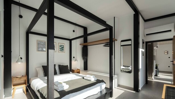 Une chambre à coucher moderne avec un lit à baldaquin, une table de chevet, une petite commode, un miroir fixé au mur et une petite plante en pot.
