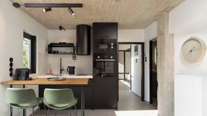 Une cuisine moderne dotée d’un îlot central, de deux tabourets de bar verts, d’un four encastré et d’un réfrigérateur noir.
