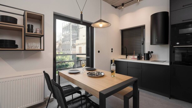 A modern kitchen with a dining table, black chairs, and a window overlooking a cityscape. - 2BR Suite Apt • Acropolis Rooftop Views • By Metro (Athens)