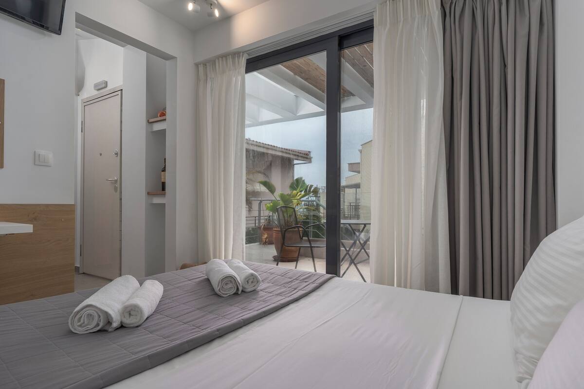 A hotel room with a bed, a bathroom, and a balcony with a view.