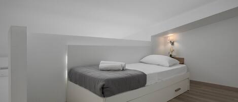 A modern, minimalist bedroom with a single bed, a nightstand, and a wall-mounted light fixture.
