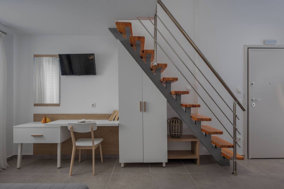 A modern room with a desk, chair, and a staircase with wooden steps and metal railings.