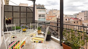 A balcony with a table and chairs, potted plants, and a view of the cityscape.