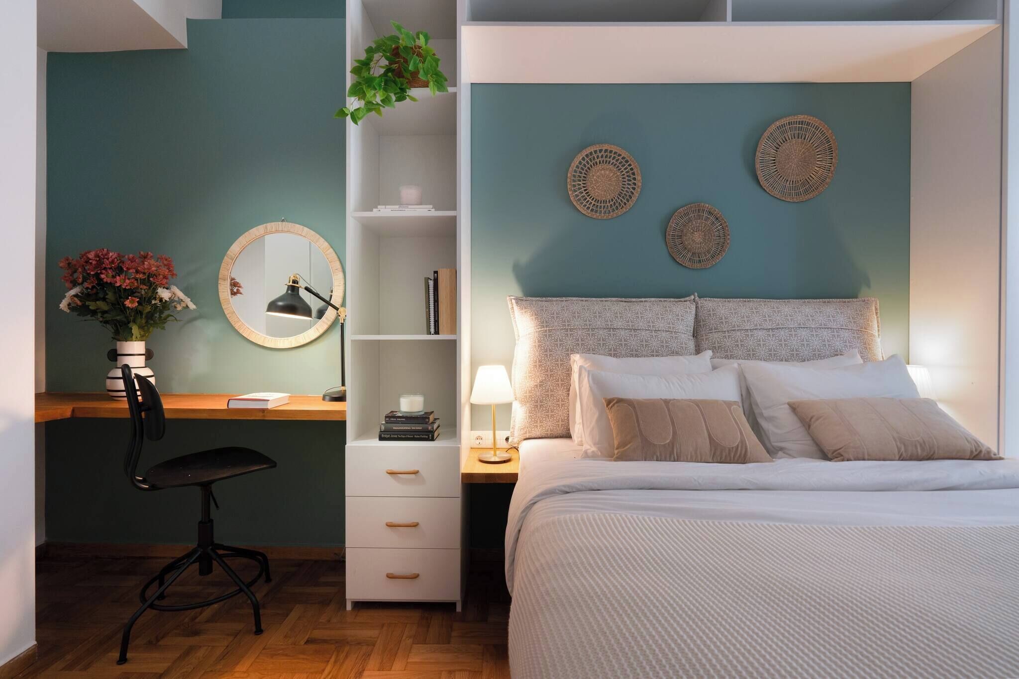 A bedroom with a bed, a desk with a chair, a nightstand, and a wall-mounted shelf.