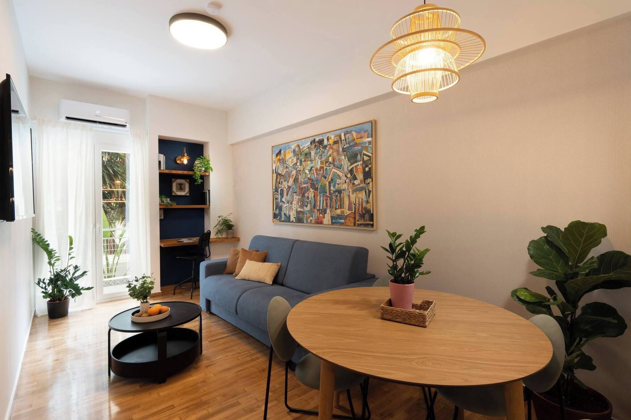 A modern living room with a blue sofa, a round wooden table, and a large abstract painting on the wall.