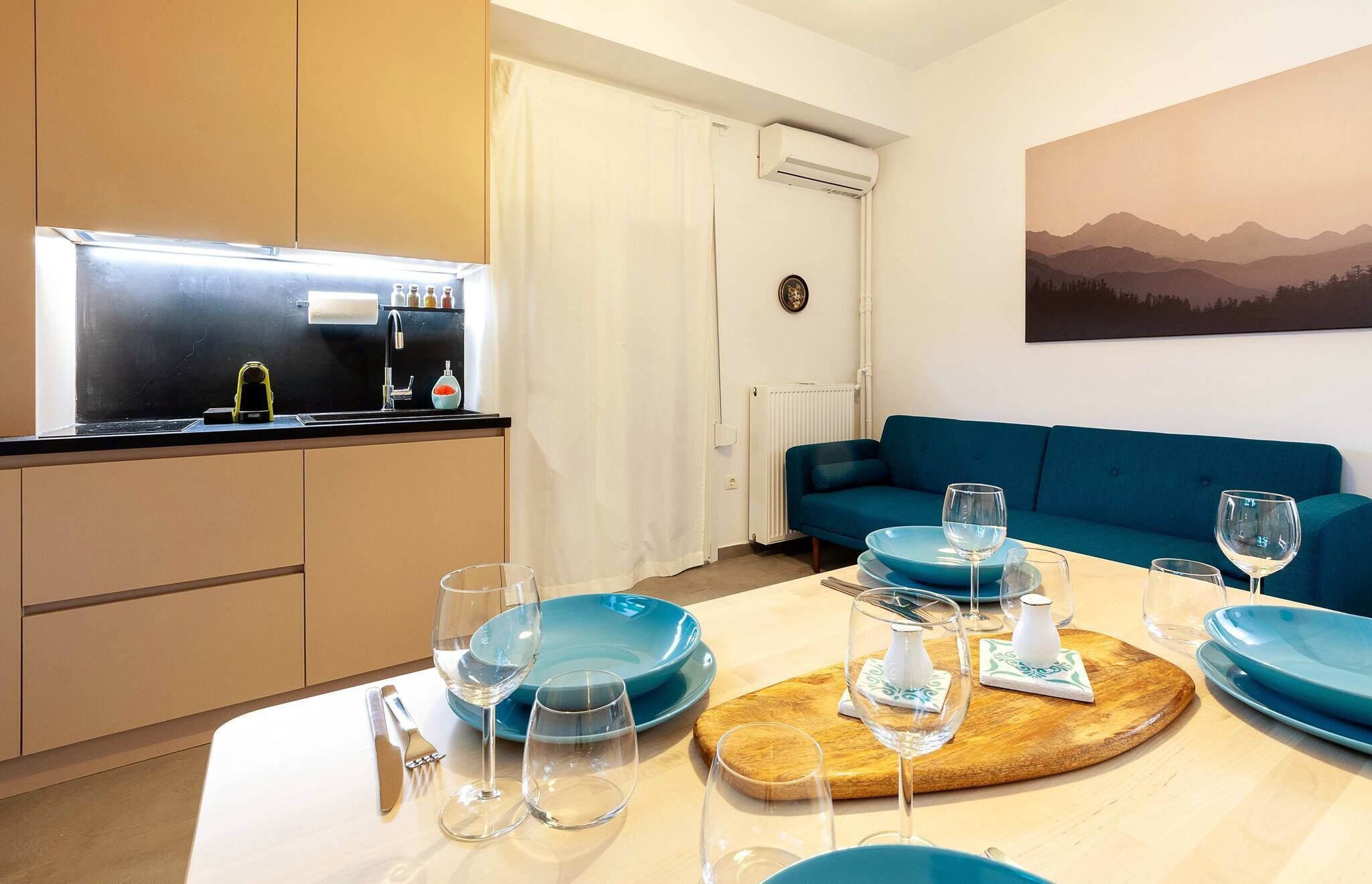 A modern kitchen with a built-in stove, a dining area with blue plates and glasses, and a blue sofa in the living room.