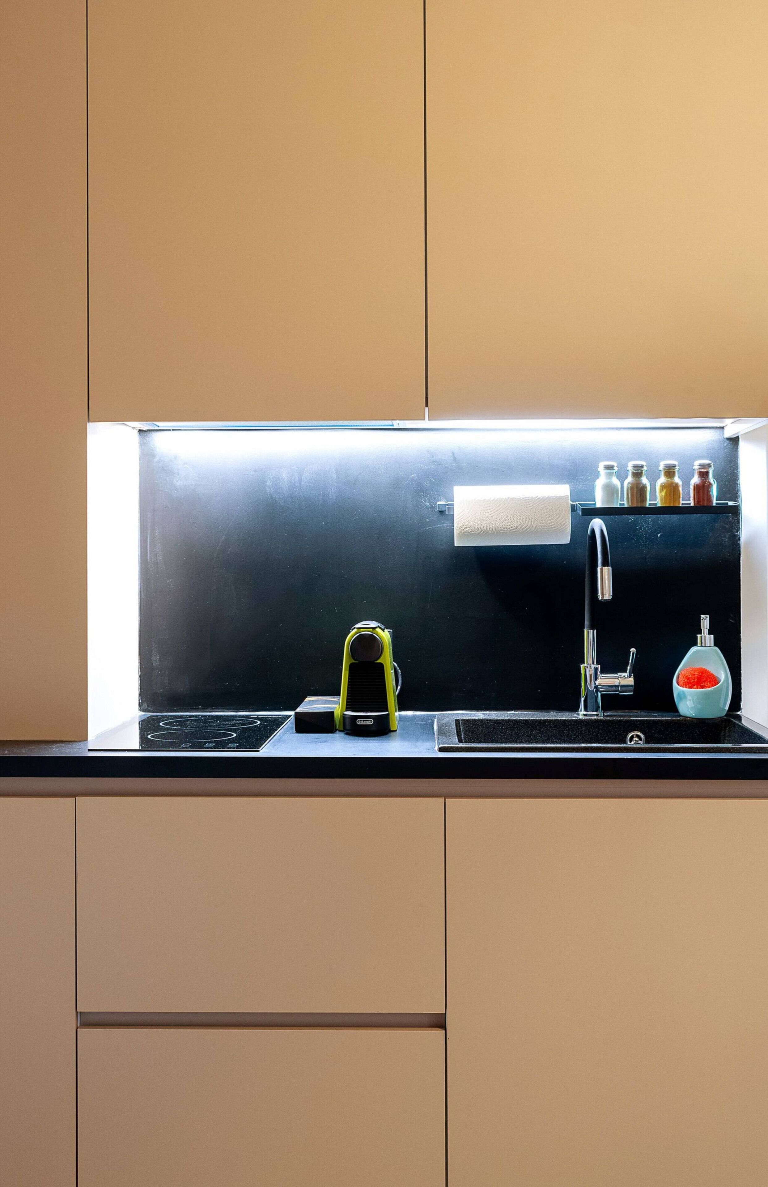 Een keuken met een zwart aanrecht, een geel apparaat, een zwarte kraan en een zeepdispenser.
