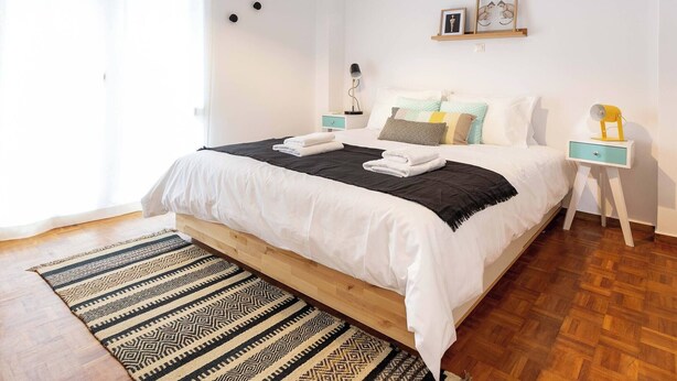 A bedroom with a bed, bedside tables, a lamp, a wall-mounted air conditioner, and a window with curtains.