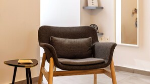 A modern armchair with a cushion, a small side table with a book, and a wall-mounted shelf with decorative items.