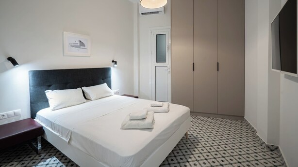 A neatly arranged hotel room with a large bed, a bedside table, a wardrobe, and a hanging light fixture. - Urban Escape: Exarcheia Remodel (Athens)
