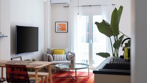 A modern living room with a flat-screen TV, a sofa with yellow pillows, a glass coffee table, and a large plant. - Urban Escape: Exarcheia Remodel (Athens)