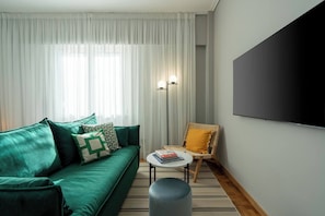 Una sala de estar con un sofá verde, una pequeña mesa redonda con libros, una silla amarilla y una lámpara de pie.